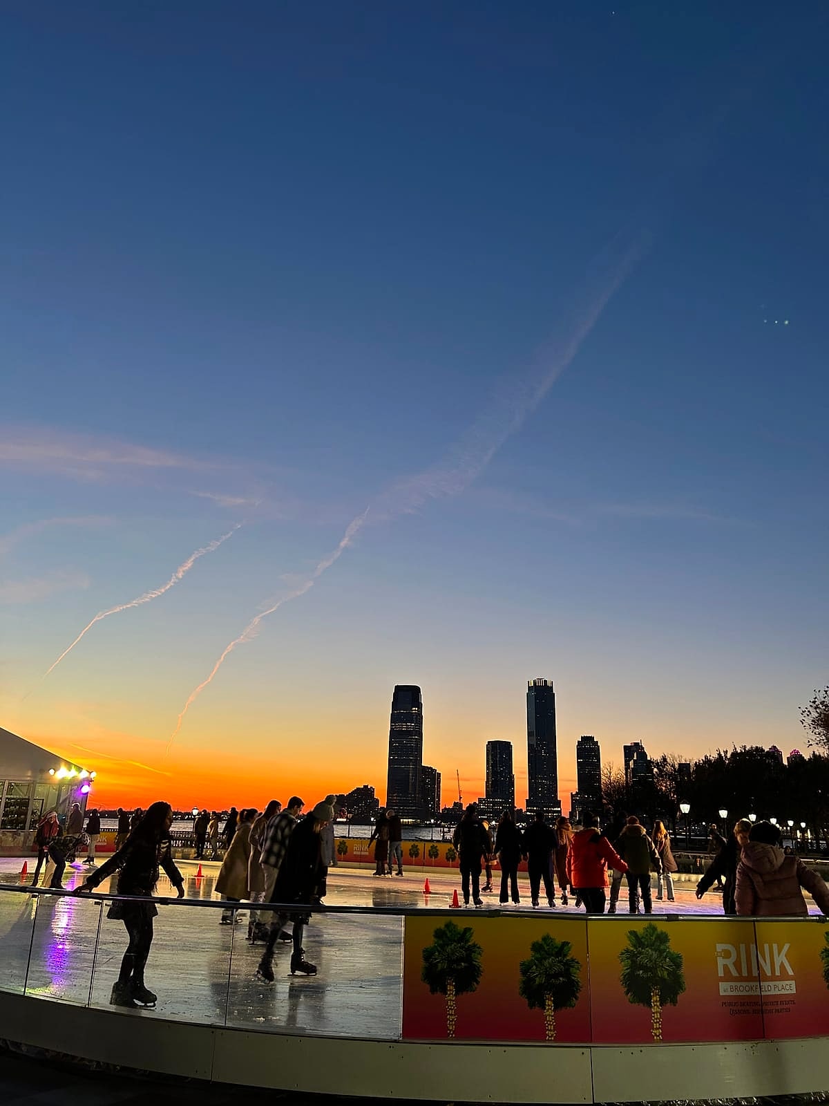 Skaters on the rink at Brookfield Place at sunset, with the river behind