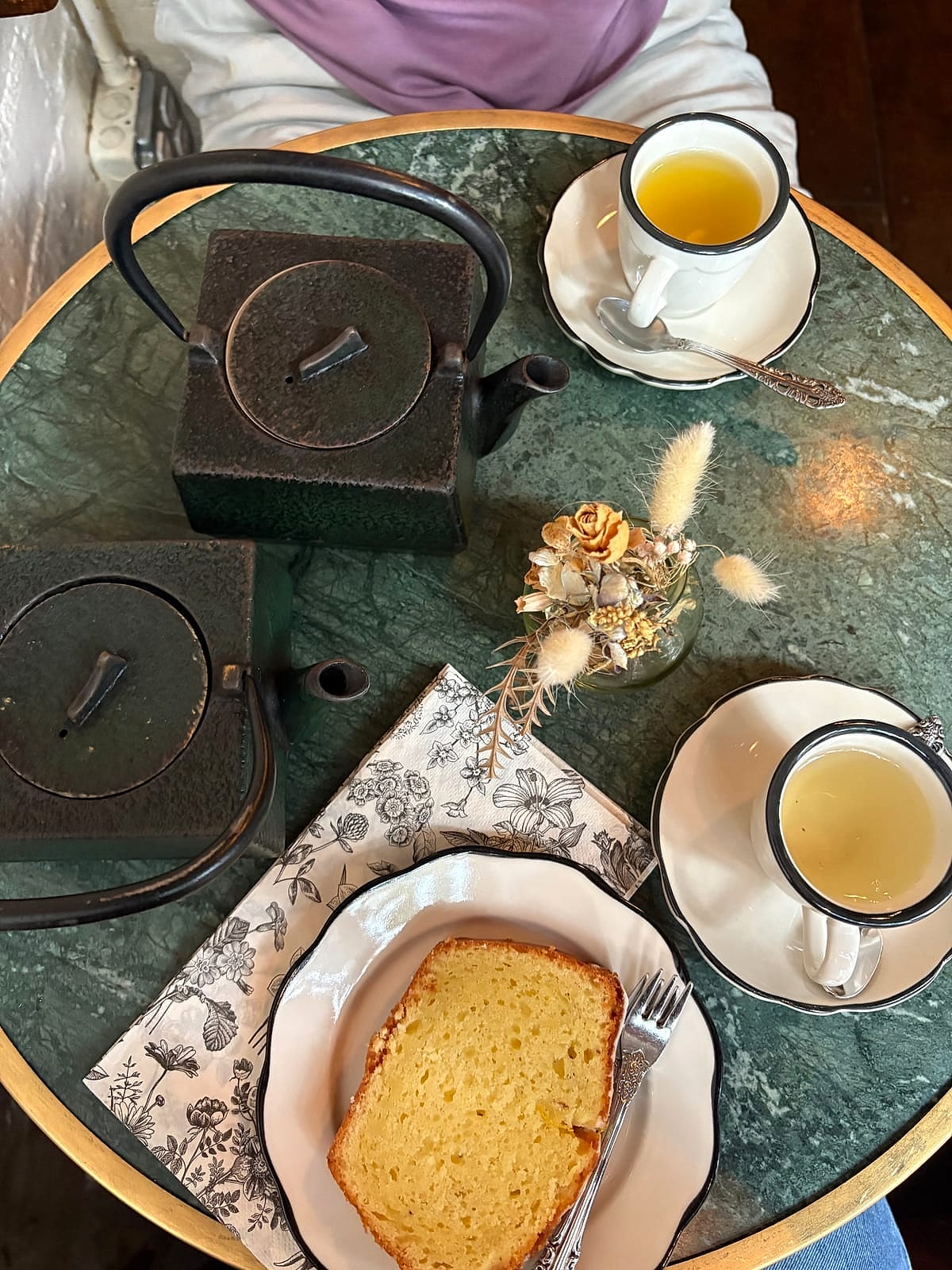 Iron teapots, cups of tea and a slice of cake on a green marble table