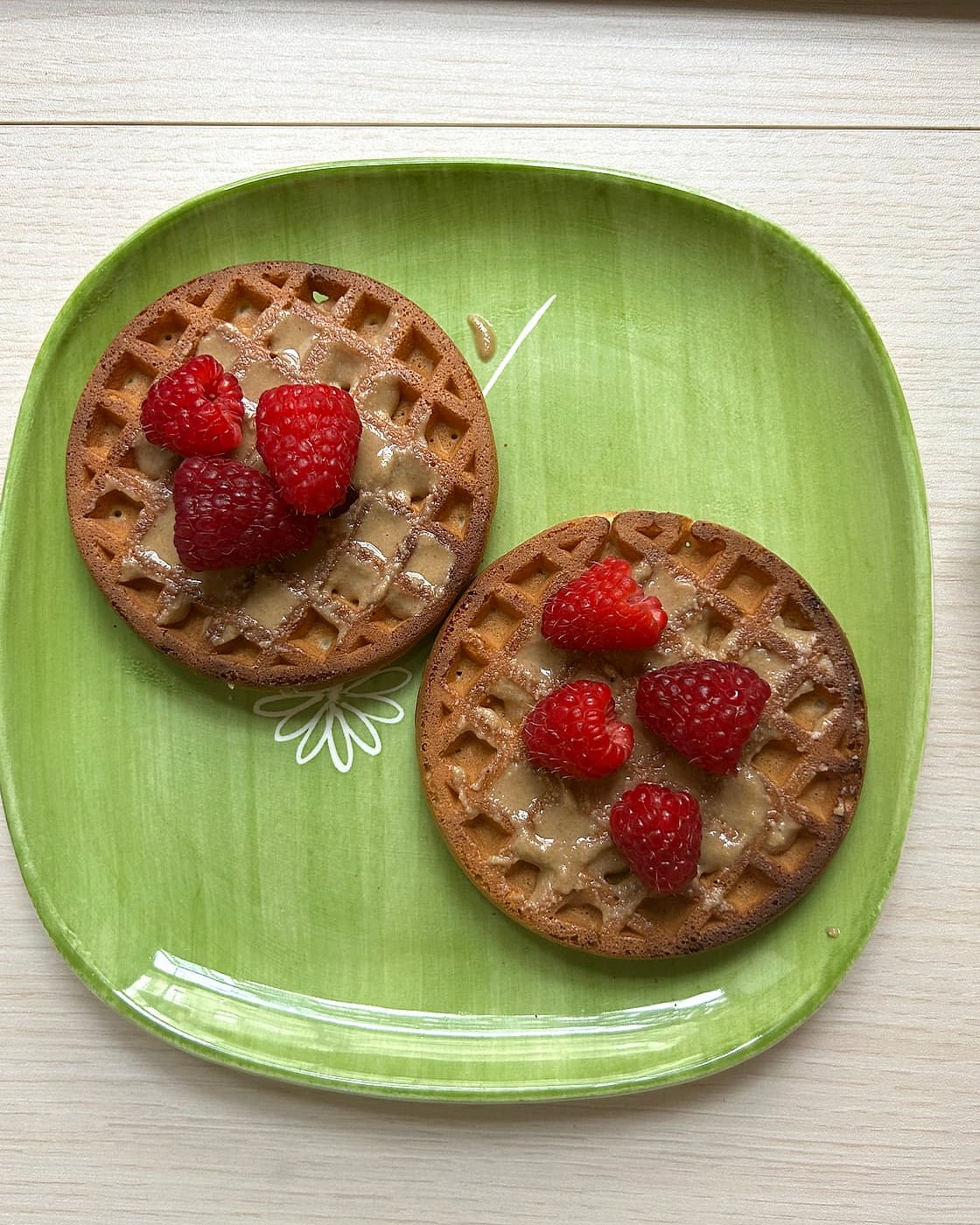 Two protein waffles spread with nut butter and topped with raspberries on a green plate