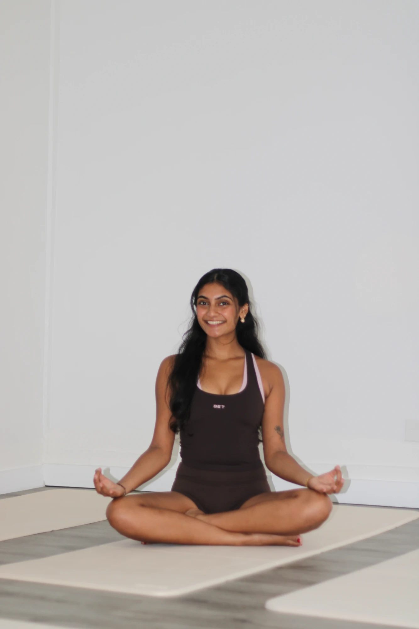 Saniya sitting cross-legged on a yoga mat in easy pose, smiling